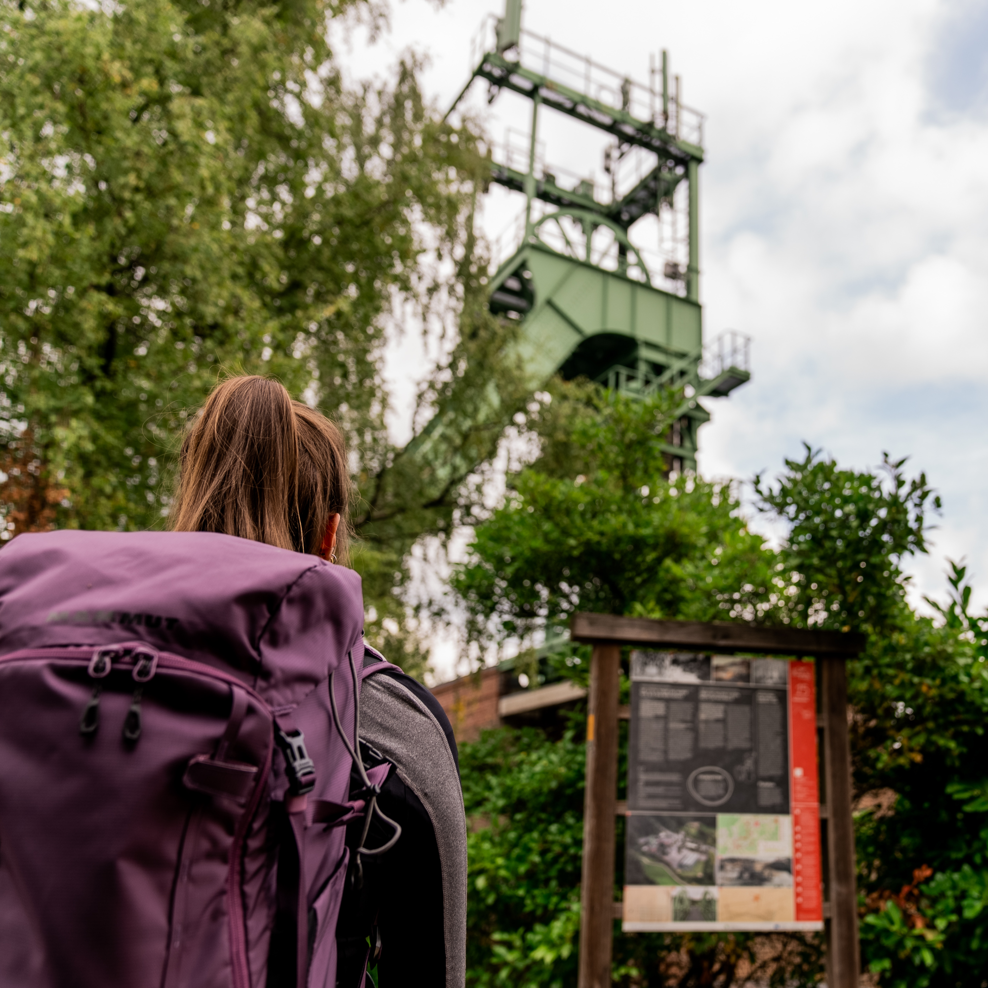 Wanderin steht vor einem Fördergerüst mit Info-Tafel davor