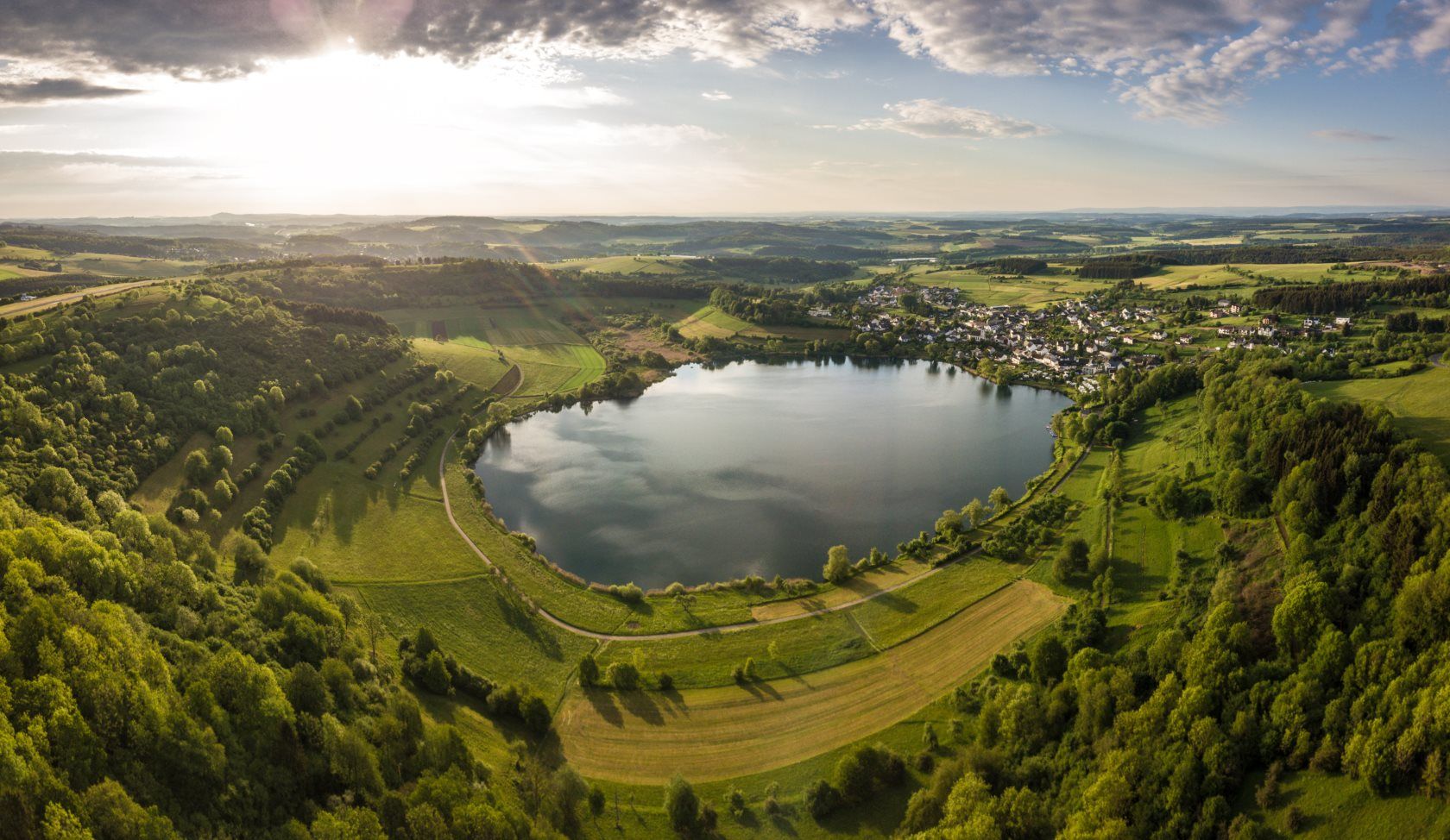 Kreisrunder See in einer grünen Landschaft aus Wiesen und Feldern