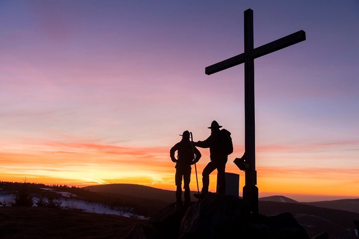 Zwei Männer am Gipfelkreuz im Gegenlicht des Abendrots