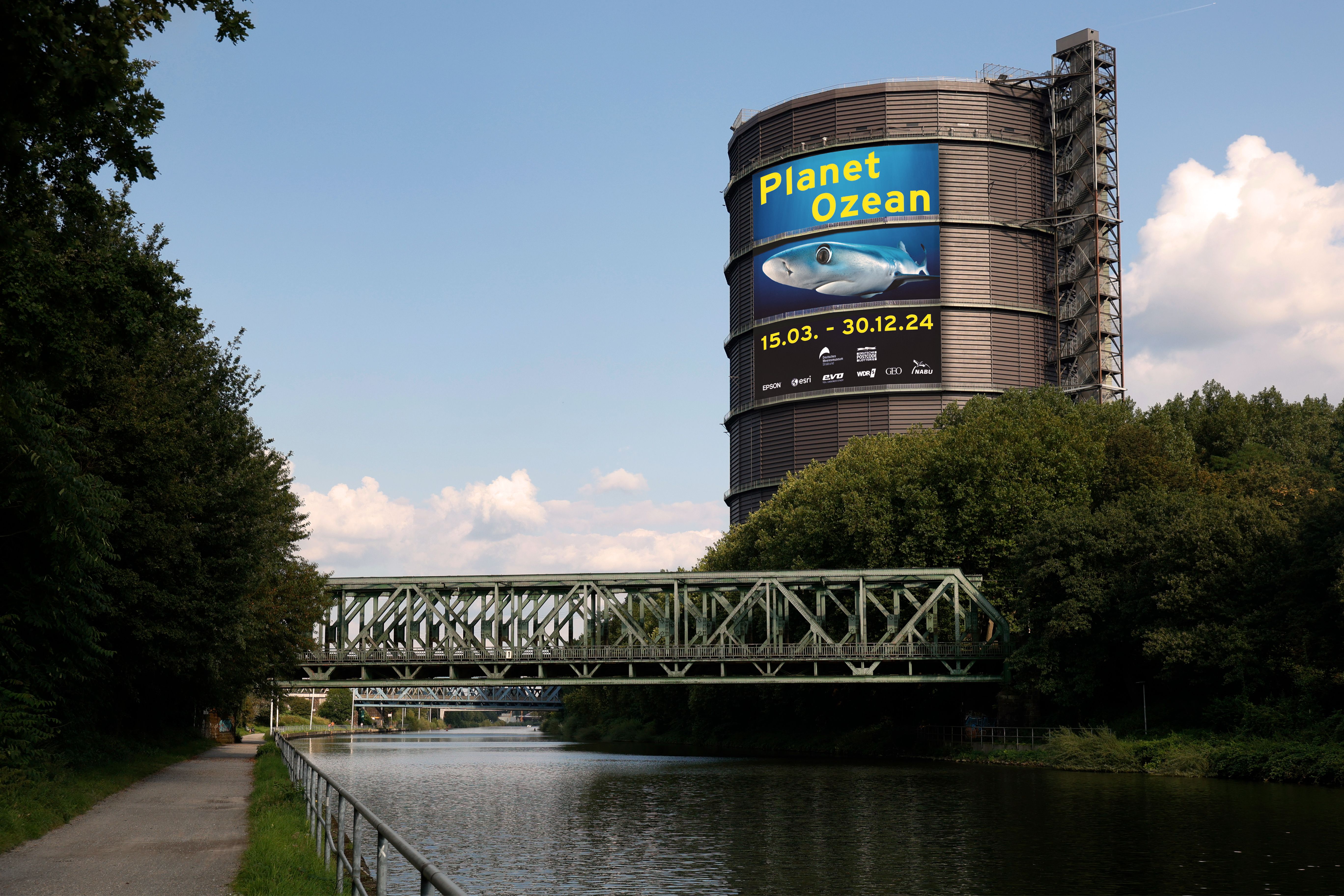 Ein großes Plakat deutet am Rhein-Herne-Kanal auf die Ausstellung Planet Ozean im Gasometer hin