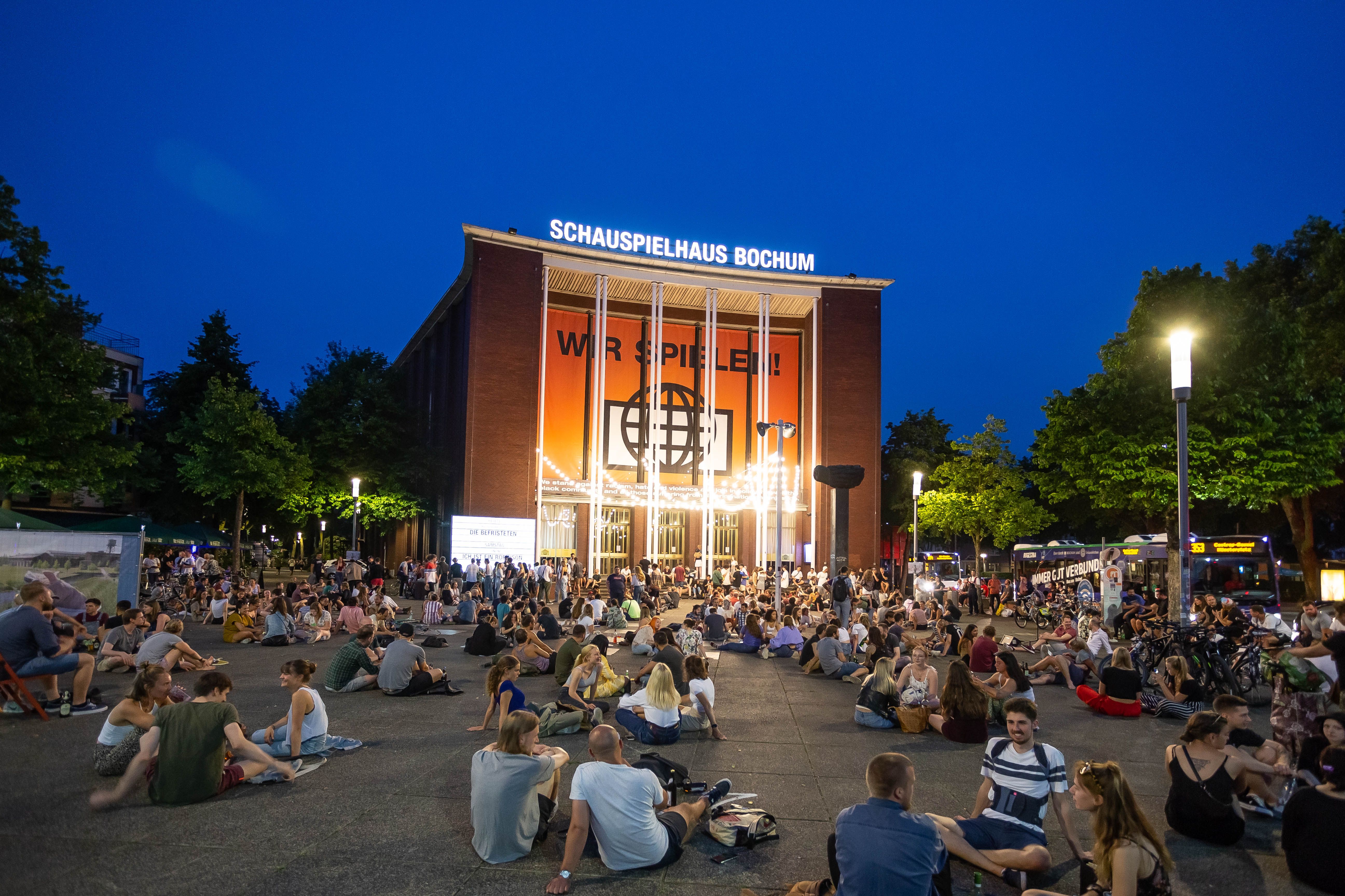 Junge Menschen sitzen vor dem Schauspielhaus Bochum und unterhalten sich